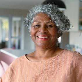 Senior woman in peach colored shirt smiling at home