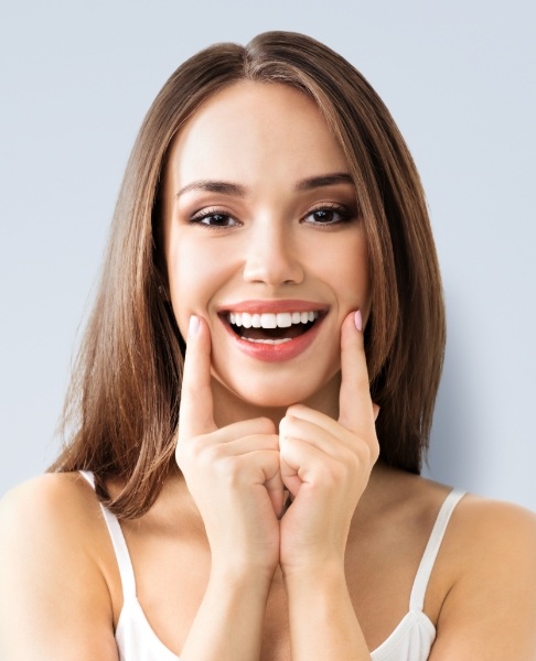 Woman pointing to smile after metal free dental restorations