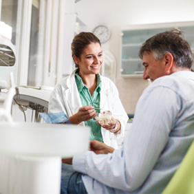 Smiling dentist showing patient model of teeth