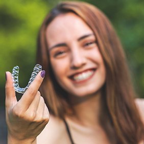 Girl with purple nails outside holding Invisalign with thumb and forefinger