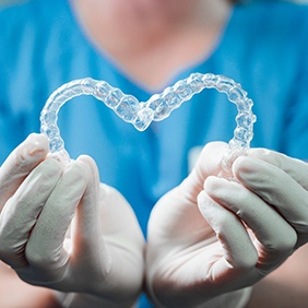 Dentist in blue scrubs holding Invisalign in a heart shape