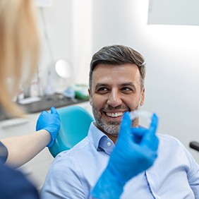Man in collared shirt smiling as dentist approaches with Invisalign
