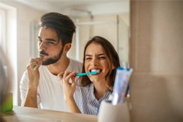 Couple looking at reflection while brushing their teeth in bathroom