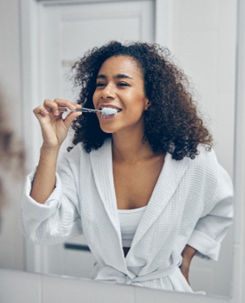 A beautiful woman brushing her teeth in front of a bathroom mirror