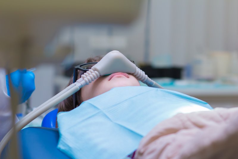 Person with glasses laying on dental chair wearing a dental bib and gas mask