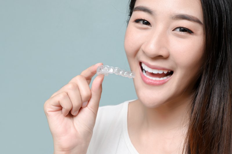person smiling while holding Invisalign aligner